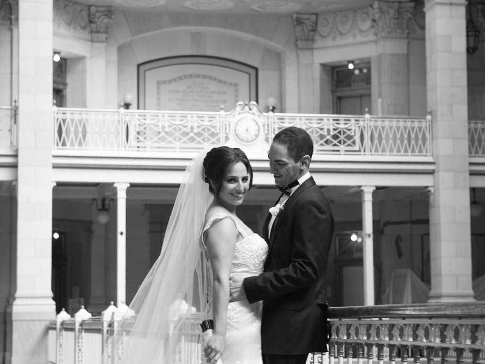 A Muslim couple have an opulent wedding ceremony at the Society Room with large family and many friends at beautiful hotel in Hartford, Connecticut. Bride and groom pose for pictures with a boquet of white roses flowers.