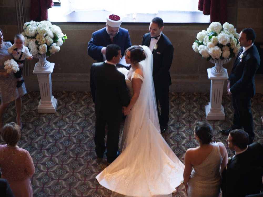 A Muslim couple have an opulent wedding ceremony at the Society Room with large family and many friends at beautiful hotel in Hartford, Connecticut. Bride and groom look at each other as wedding officiant performs ceremony at the Society Room.