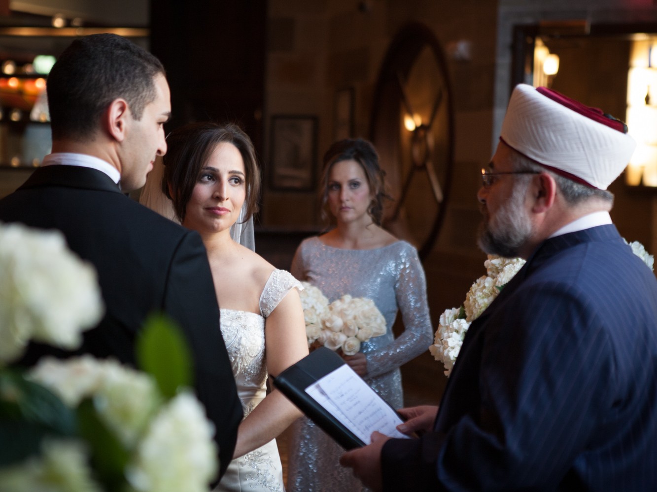 A Muslim couple have an opulent wedding ceremony at the Society Room with large family and many friends at beautiful hotel in Hartford, Connecticut. Bride and groom look at wedding officiant as he performs ceremony at the Society Room.