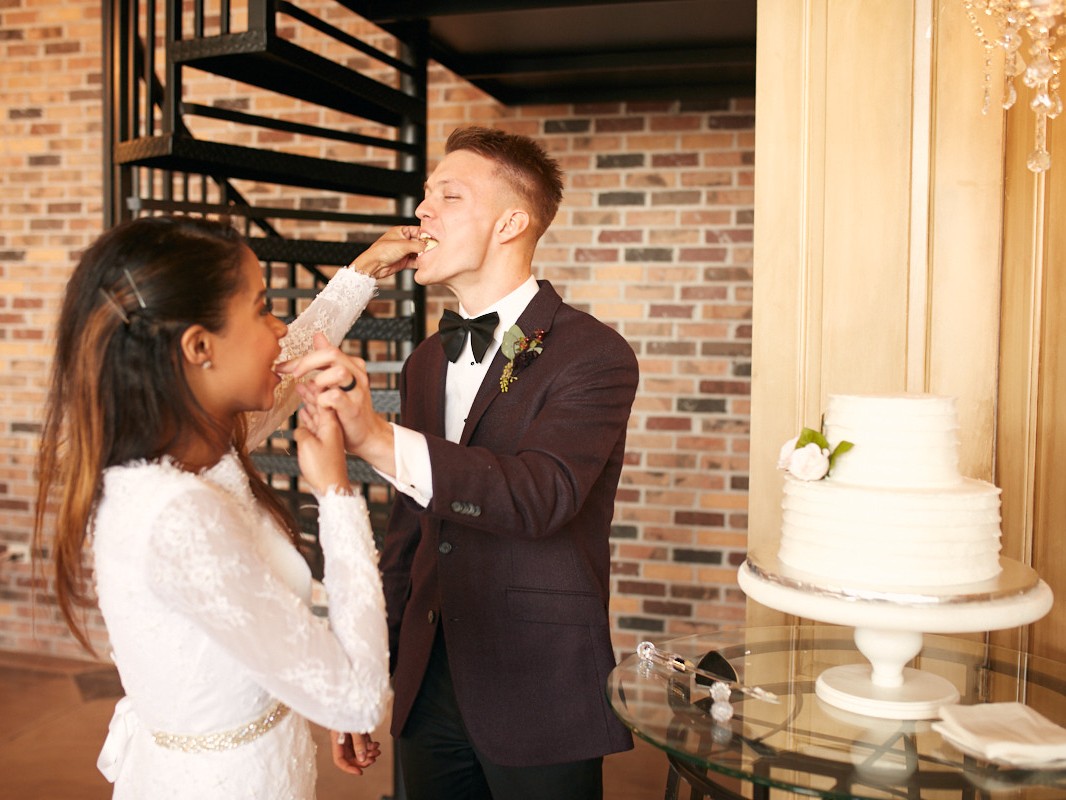 Bride and groom shove wedding cake into each other's mouths at reception